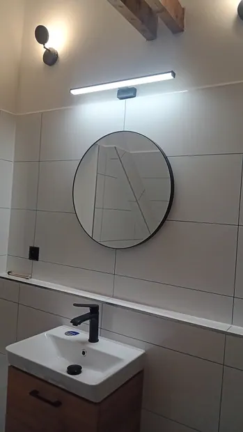 Umyvadlo s osvětleným zrcadlem pod přiznanými trámy.