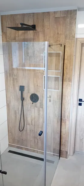 Hotová sprcha se skleněnou zástěnou a černou sprchovou sestavou.