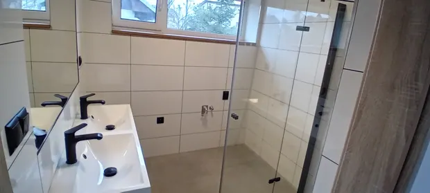 Celkový pohled na světlé obklady, dvojumyvadlo a sprchový kout.