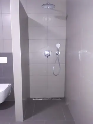 Sprchový kout s liniovým odtokem a navazující závěsné WC.