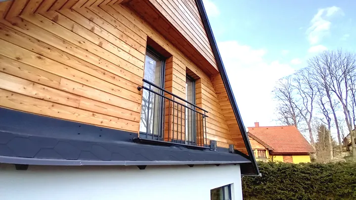 Detail dřevěného obkladu štítu, oken a klempířských prvků.