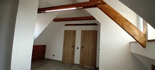 Pokoj s přiznanými dřevěnými trámy a interiérovými dveřmi.