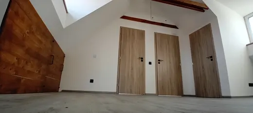 Dřevěný obklad stěny, přiznané trámy a dveře v podkroví.