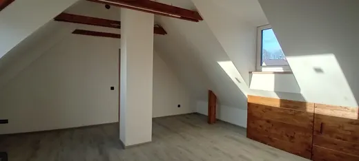 Světlý obytný prostor se střešními šikminami, dřevěným obkladem a vinylovou podlahou.