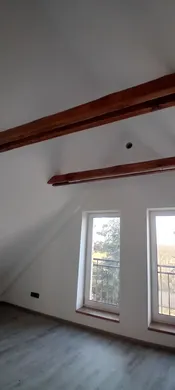 Střešní šikmina, přiznané dřevěné trámy a okna hotového bytu.