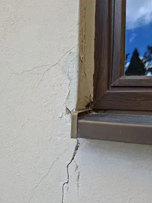 Praskliny omítky v okolí okna před opravou.